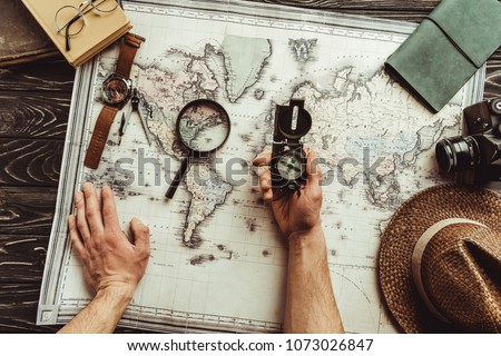 partial view of man with compass at tabletop with map, magnifying glass, photo camera and hat