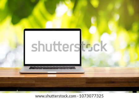 Laptop blank screen on wooden table in green garden blurred lens background