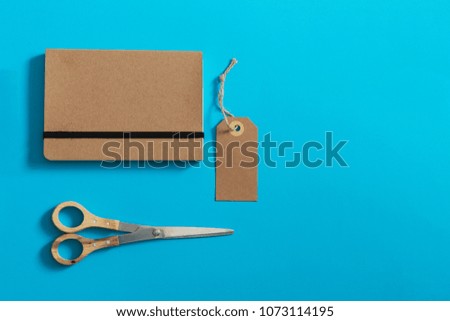 Brown eco label, notebook and scissors with wooden handles on a bright colored background. Mockup.