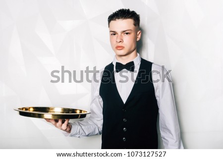 Portrait of male waiter who is holding tray in hall of restaurant.Portrait of waiter with serving tray meeting restaurant guests