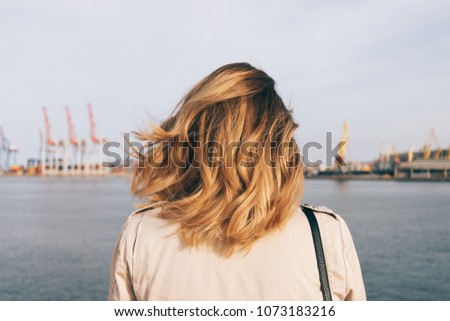 Close-up female head with golden honey color curly hairstyle watch at the seaport. Rear view young woman looking at the sea. Royalty-Free Stock Photo #1073183216