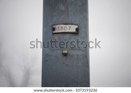 An old number plate saying 1107 on a grey iron post.