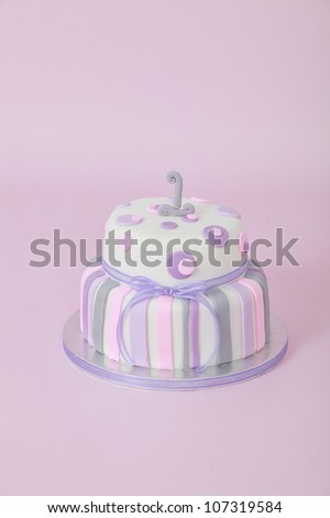 Beautifully designed and decorated girls double tier round birthday party cake with white fondant icing and purple and pink stripes and circular polka dots with number one isolated on pink background