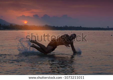 Male silhouette jumping in the water at the sea at sunset