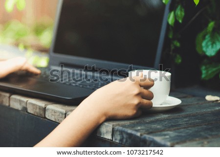 Women hands holding a cup of coffee and using a laptop