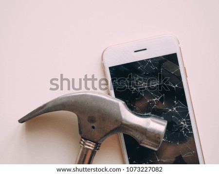 broken screen of smartphone with hammer on white table.