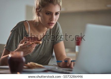 Stressed young businesswoman eating and working on laptop at home.