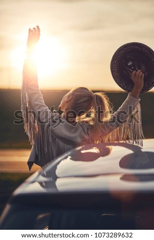 Woman in car stretches arms out of the window.