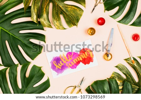 Monstera leaves and hand lettered sign Hello Summer with various stationary accessories: brushes, scissors etc. Vacation concept, flatlay, pastel background
