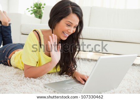 Beaming Latin woman on a video chat while lying on the floor. Working from home in quarantine lockdown. Social distancing Self Isolation Royalty-Free Stock Photo #107330462