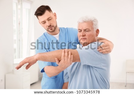Young physiotherapist working with senior patient in clinic Royalty-Free Stock Photo #1073345978