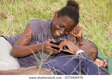 Happy couple lying on green grass laughing and smiling while using mobile phone.