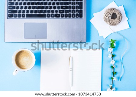 Creative workplace with laptop, notebook, envelopes, twine and flowering branch on a blue background. Spring concept
