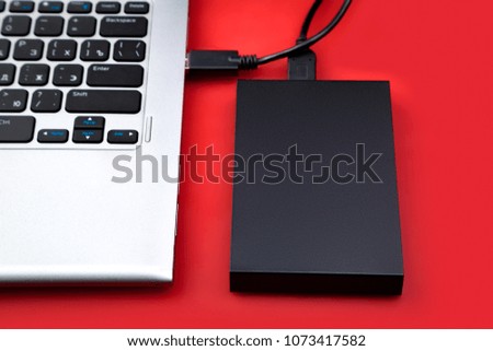 A portable hard drive connected to a laptop on a red table. The concept of data storage