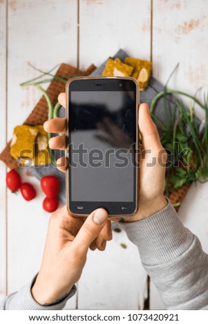 Smartphone food photography vegetable salad in bowl of tomatoes, cucumbers, oil. Woman hands take phone photo of dinner or lunch for social networks. Blank screen Raw vegan vegetarian healthy food