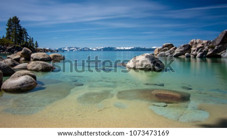 Sand Harbor at Lake Tahoe North, Nevada county, California, USA, featuring blue transparent water, rocky shore and snow on tops of background mountains on a blue sky day with few clouds Royalty-Free Stock Photo #1073473169