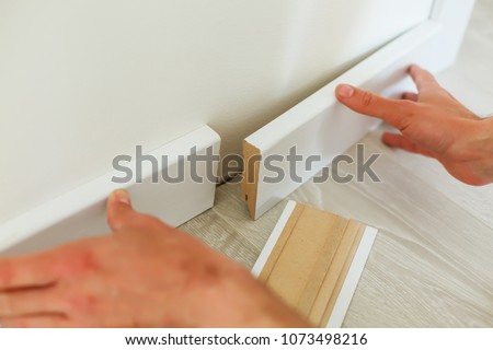 Mans hands putting white baseboard, do it yourself Royalty-Free Stock Photo #1073498216