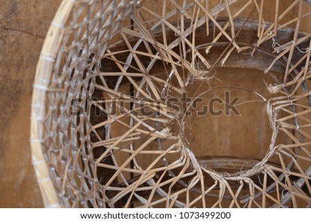Close up view of an ancient braided basket used in France to catch fishes. Circular object with holes exposed on an old wooden chair. Vintage design. Geometric clear brown shapes. 