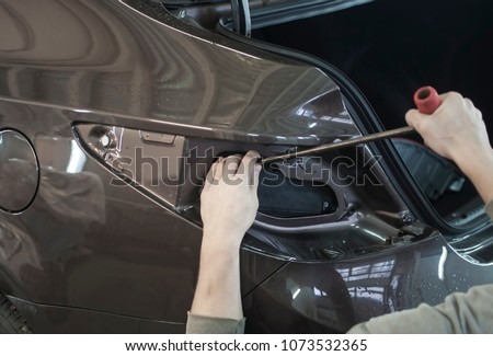 Body repair. The mechanic at the auto shop with tools to repair dents in car body Royalty-Free Stock Photo #1073532365