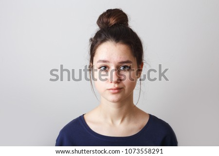 portrait of a pimply teenage girl in a blue T-shirt on a gray background, sad doubting face Royalty-Free Stock Photo #1073558291