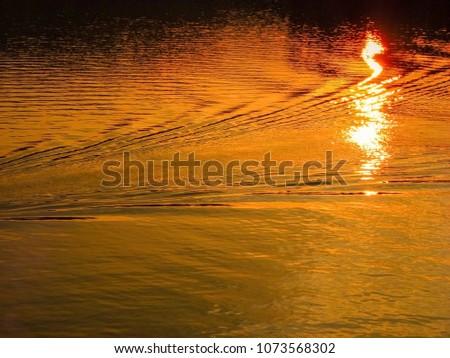 Beautiful sunset over the lake with light reflection on the water in gold colour.