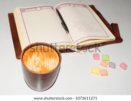 A photo of a cup of coffee with colored candy and a notebook. A saturated coffee color with an airy foam and a bright aroma.
