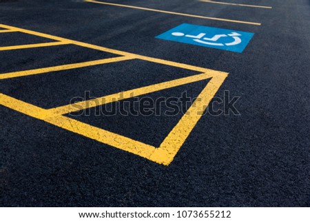 Handicap parking icon on parking lot asphalt with yellow painted lines.
