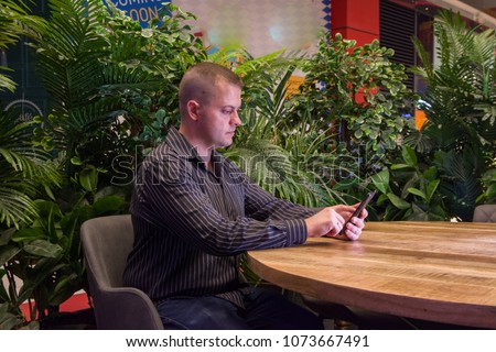 man in a black shirt sitting in a summer cafe and emotionally communicates by phone. 
