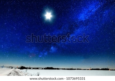 Moon and milky way over a snowy field.