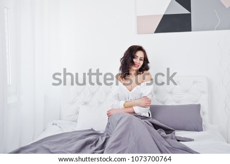 Studio portrait of brunette girl in white blouse lying on bed.