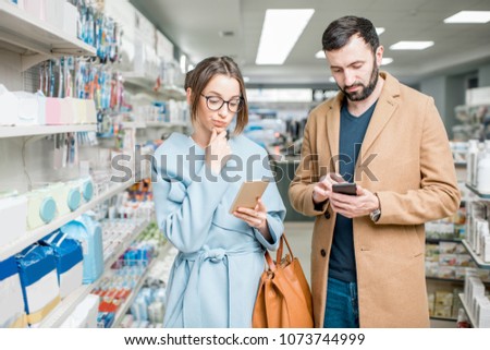 Young couple dressed in coats choosing medicine standing with phones in the pharmacy store