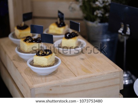 a piece of cheese Cake toping with strawberry jam in a white cup, placed on a wooden table.
The top is decorated with small flags for text.Blank space for text input.
