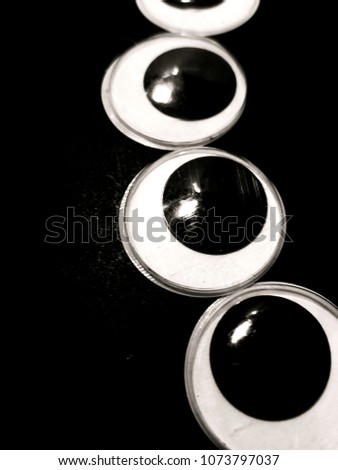 A pile of googly eyes scattered about on a black surface. Isolated. Macro shot. Closeup. Craft object. Paranoia Concept.