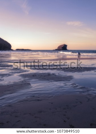 View across the sands to Gull Rock, Portreath, Cornwall, as the sun sets beyond the cliff.