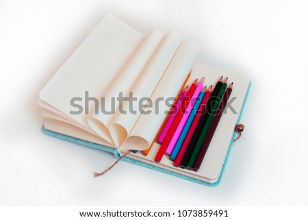 Preparation for school. Opened notebook with the pages wrapped in a circle and multi-colored pencils on a white background.