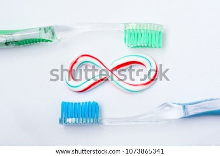 the infininy symbol is made from a three-color toothpaste and is located between two toothbrushes, close-up medical abstract background