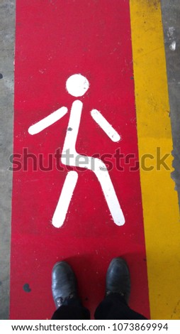 A man with old shoes is walking following walk sign on the red walk way in the factory, Safety road.

