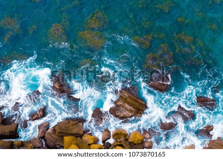 Top aerial view of blue waves crashing on rocky Australian coastline. Summer seascape with birds eye view shot over ocean waves and cliffs. Travel concept background