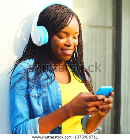 Beautiful african woman with headphones listens to music using smartphone in the city
