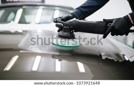 Car detailing - Man with orbital polisher in repair shop polishing car. Selective focus. Royalty-Free Stock Photo #1073921648