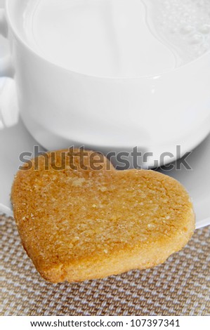 closeup of a cup of milk and a heart-shaped cookie