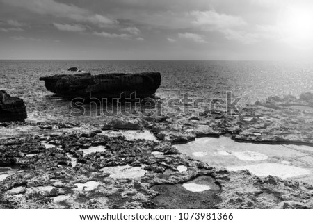 Gozo is a small island of the Maltese archipelago in the Mediterranean Sea.  Rugged coastline delineated by sheer limestone cliffs, and dotted with deep caves at sunset. Black and white picture