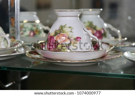 Antique and vintage floral bone china teacups and saucers through clear glass cabinet with blurred background Royalty-Free Stock Photo #1074000977