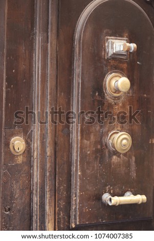 Close up outdoor view of several handles fixed at an ancient wooden door. Vintage style with circular and horizontal golden iron objects placed on a brown textured surface. Old decorative elements. 