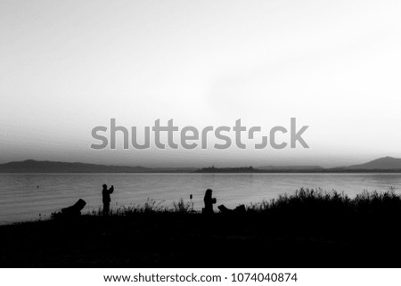 Silhouettes of a couple on a lake shore, taking photos of sunset