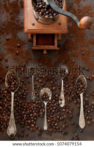 Close-up photo of metal spoons with aroma coffee beans and coffee bean grinder on black table background