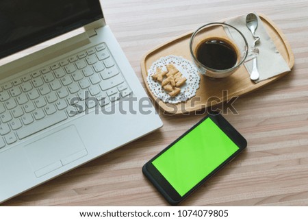 smart phone green screen with cup coffee and computer on wooden table top view.