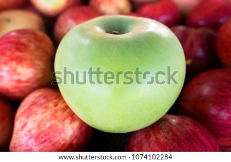 one  green apple among group of many red apples .