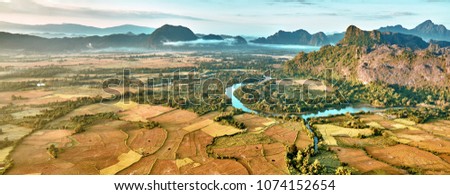 Aerial bird's-eye sunrise time view on valley landscape with karst mountains, river and rice fields. Laos, Vang Vieng.
