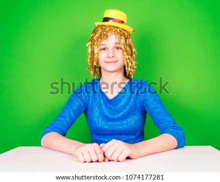 Portrait of a beautiful woman woman in a golden shiny wig sitting at a table on a green background